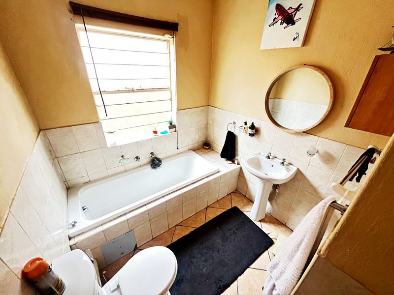 A functional bathroom featuring a bathtub, pedestal basin, toilet, and tiled finishes, offering a practical layout with natural light from a louvered window.