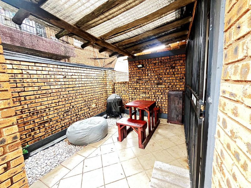A covered outdoor patio area featuring exposed brick walls, tiled flooring, and a timber-framed corrugated roof, providing a functional space for outdoor relaxation.
