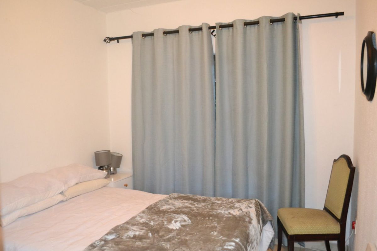 A standard bedroom featuring neutral walls and a window fitted with a curtain rod.