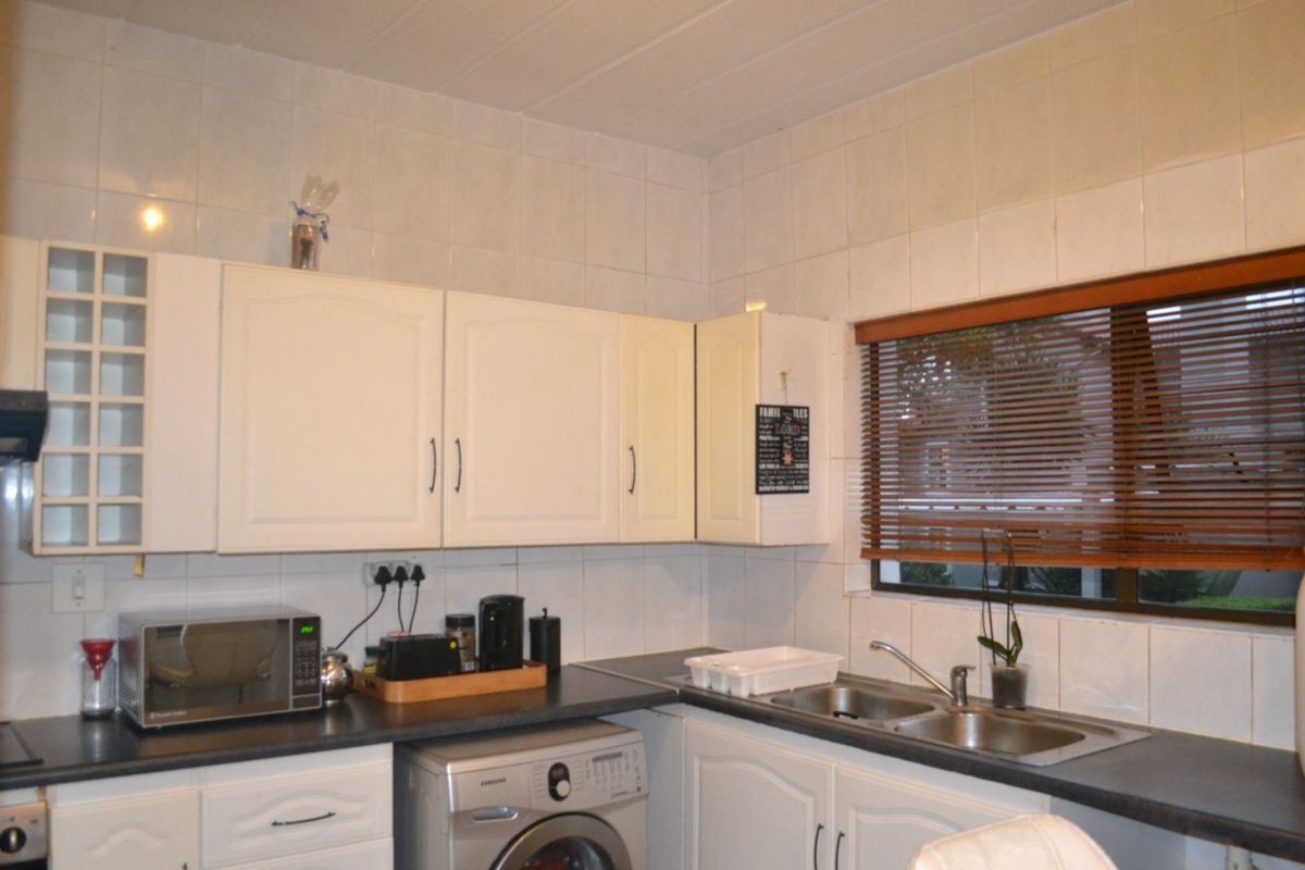 Functional kitchen featuring white cabinetry, dark laminate countertops, a double stainless steel sink, and tiled splashbacks with integrated laundry appliance space.