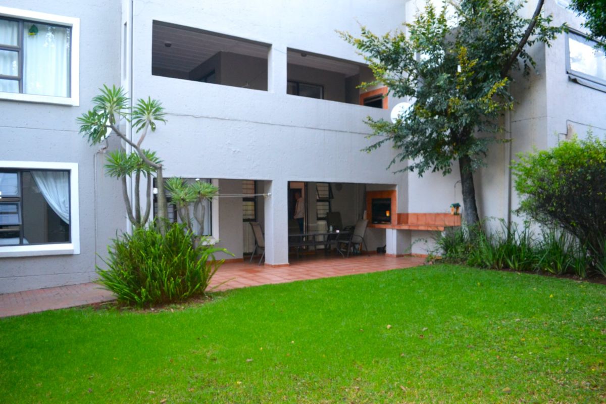 Rear view of the townhouse featuring a covered patio with a built-in braai, overlooking a private garden and lawn area.