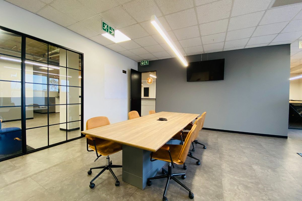 Modern commercial office meeting room featuring a black-framed glass partition, suspended ceiling with linear lighting, and neutral tiled flooring.