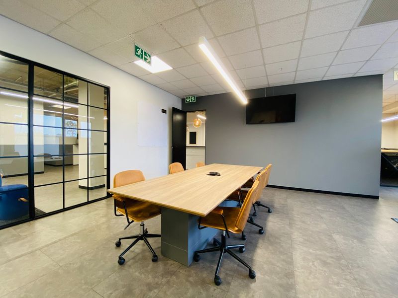 Modern commercial office meeting room featuring a black-framed glass partition, suspended ceiling with linear lighting, and neutral tiled flooring.