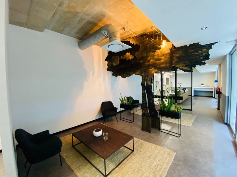 Modern commercial office reception area featuring exposed concrete ceilings, industrial HVAC ducting, and a unique decorative wooden tree partition.