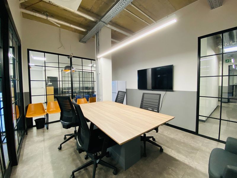 Modern commercial office space featuring industrial-style exposed ceilings, sleek black steel-framed glass partitions, and contemporary linear lighting.