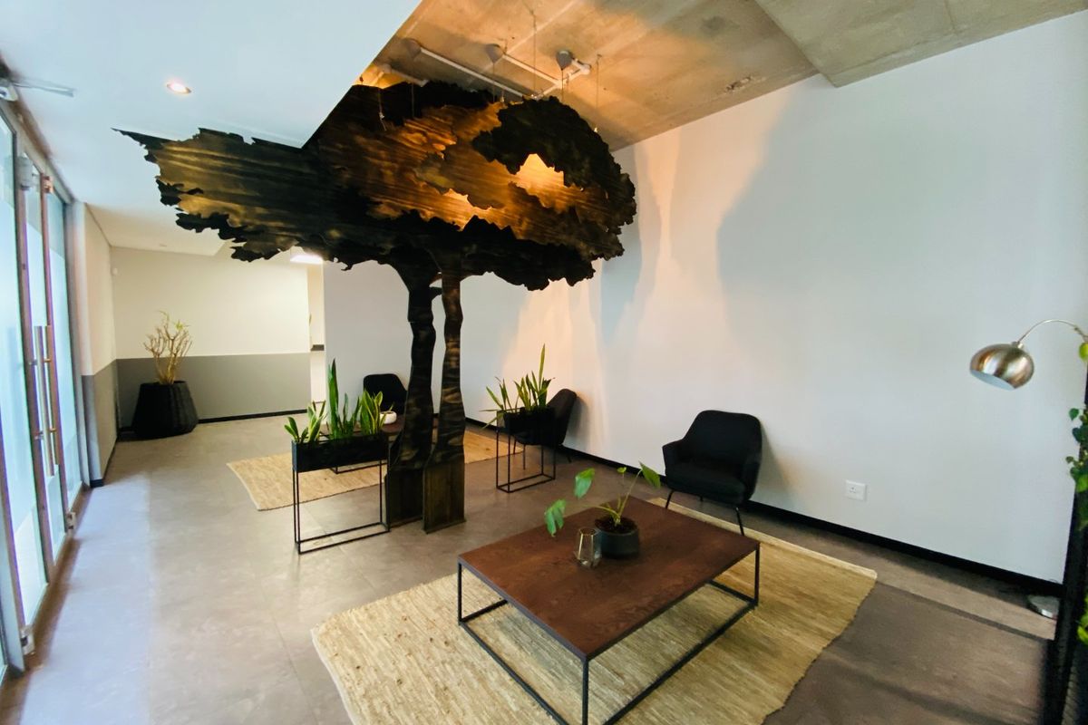 Modern commercial reception or lounge area featuring an exposed concrete ceiling, tiled floors, and a unique sculptural tree installation.