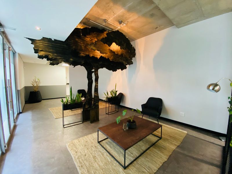Modern commercial reception or lounge area featuring an exposed concrete ceiling, tiled floors, and a unique sculptural tree installation.