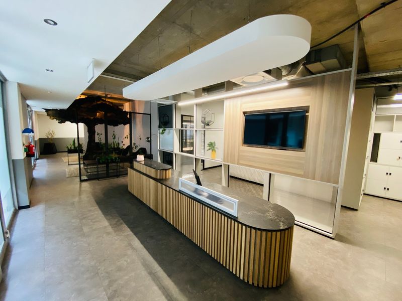 Modern commercial reception area featuring a custom curved timber-slat desk, exposed concrete ceilings, and integrated wall partitioning with built-in display and media capabilities.