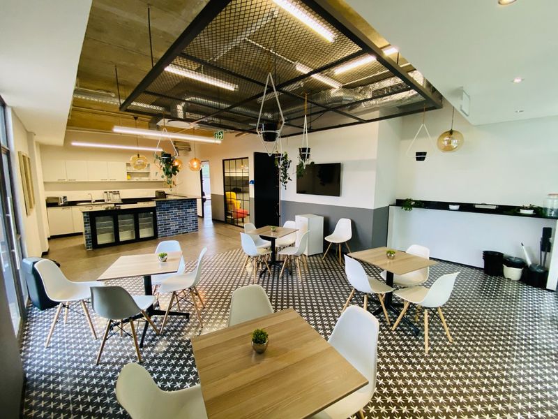 Modern open-plan commercial space featuring an industrial-style exposed ceiling, patterned flooring, and a functional kitchen area with a central island.