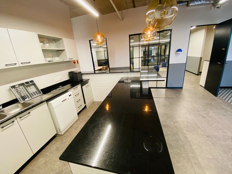 Modern commercial kitchen area featuring sleek granite countertops, ample built-in cabinetry, and a stylish glass partition wall, set against a contemporary industrial-style exposed ceiling.