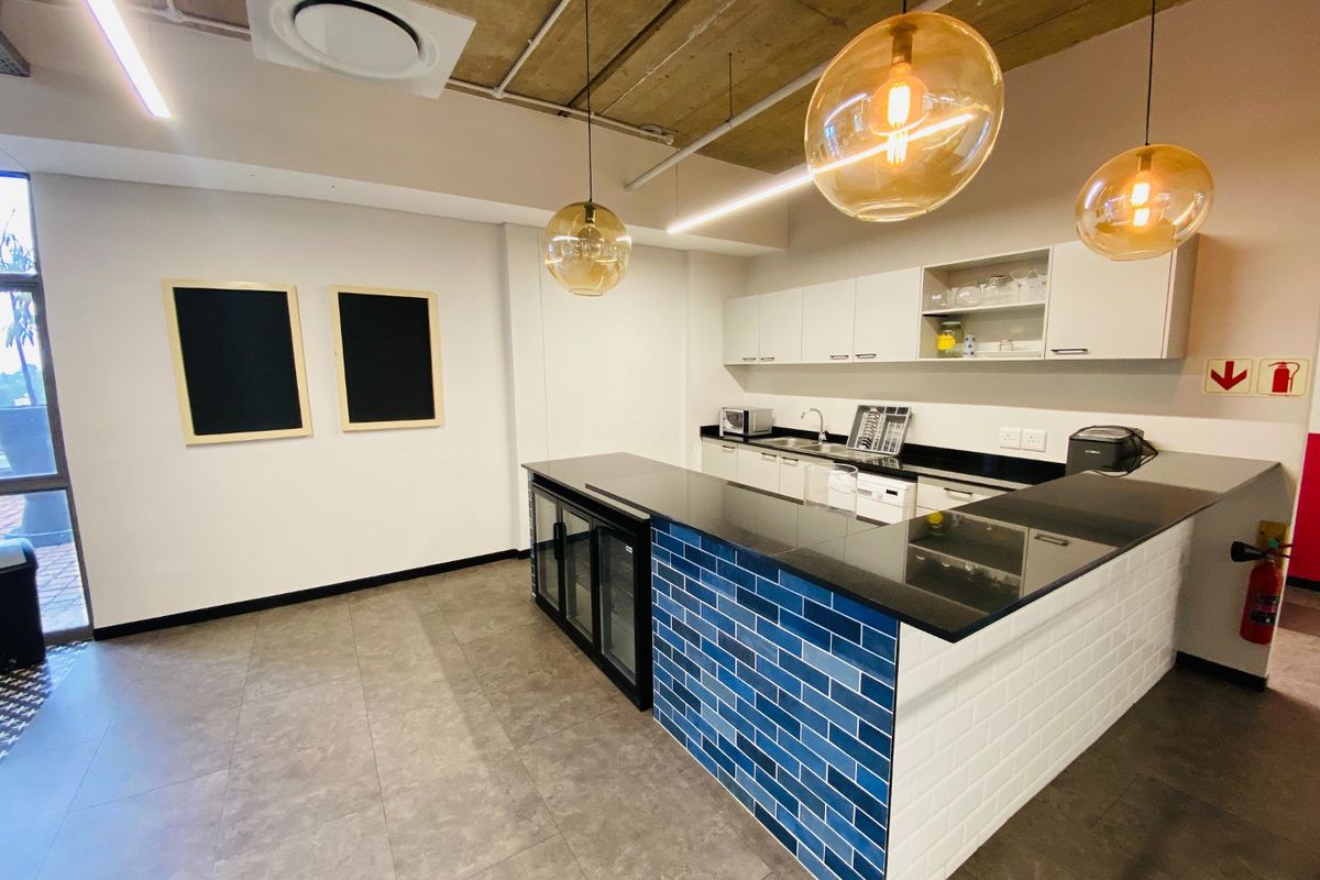 Modern commercial kitchen area featuring sleek cabinetry, granite countertops, a blue subway tile breakfast bar, and stylish pendant lighting with an exposed concrete ceiling.