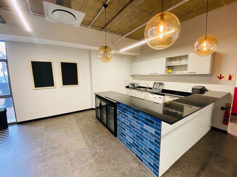 Modern commercial kitchen area featuring sleek cabinetry, granite countertops, a blue subway tile breakfast bar, and stylish pendant lighting with an exposed concrete ceiling.
