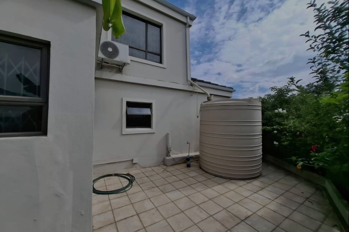 Rear exterior area featuring a tiled patio, a large water storage tank, and an external air conditioning unit mounted to the building wall.