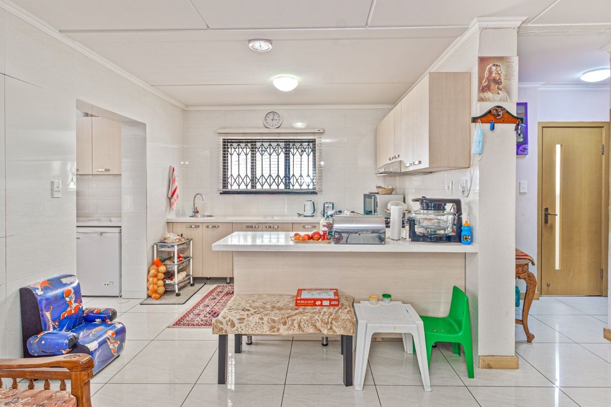 Functional kitchen featuring light-toned cabinetry, stone countertops, a breakfast bar, and tiled flooring, with an adjacent scullery area visible.