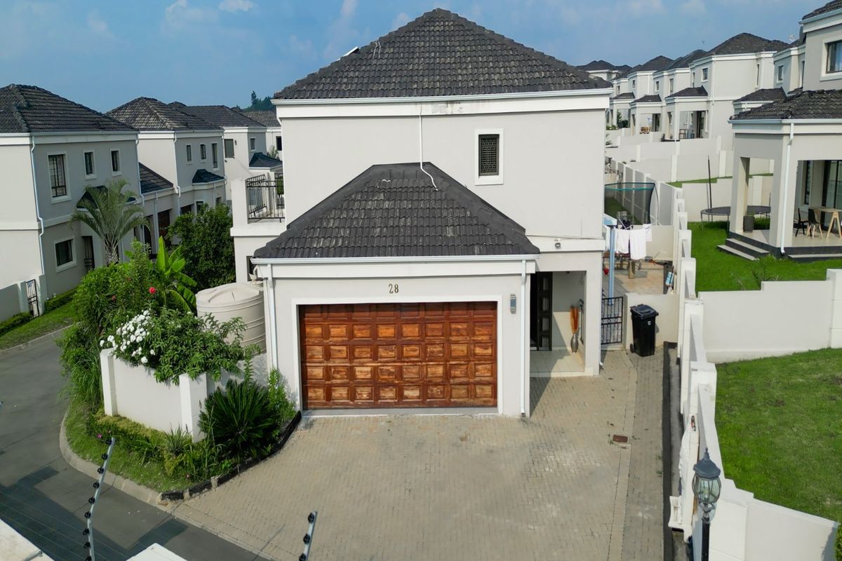 Aerial view of a two-story residential property featuring a tiled roof, paved driveway, double garage, and secure boundary walls with electric fencing.
