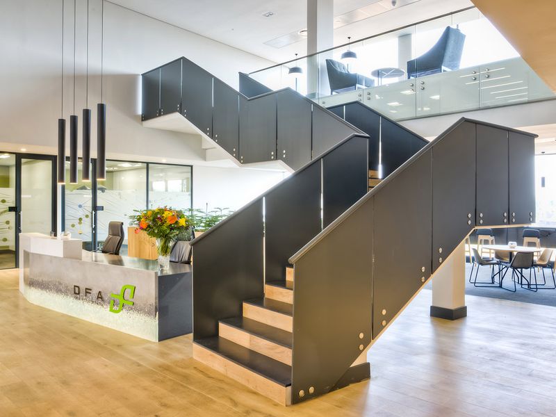 Modern commercial entrance lobby featuring a prominent central staircase, reception desk, and open-plan office layout with high-quality finishes and glass partitions.