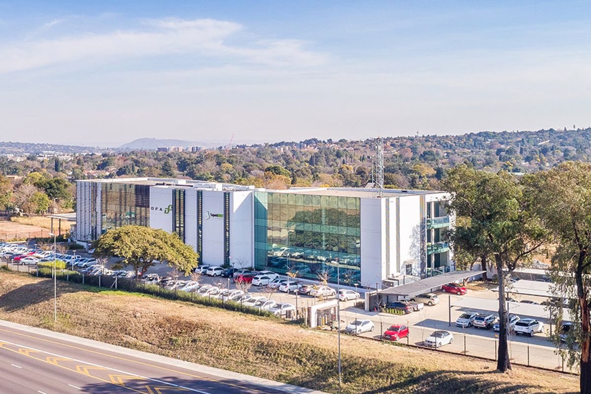 Aerial view of a modern multi-story commercial office building featuring a glass facade, extensive parking facilities, and perimeter security fencing.