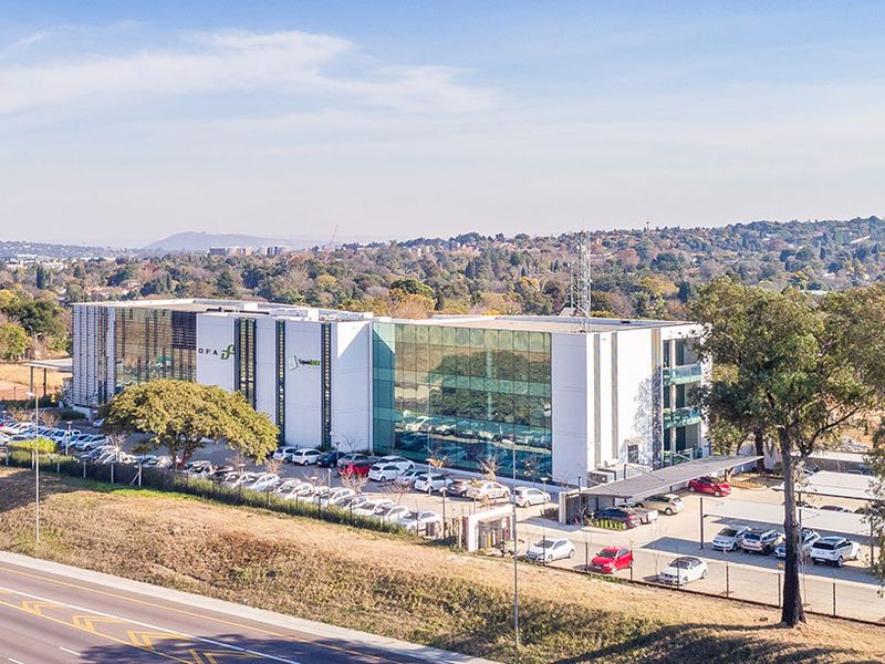 Aerial view of a modern multi-story commercial office building featuring a glass facade, extensive parking facilities, and perimeter security fencing.