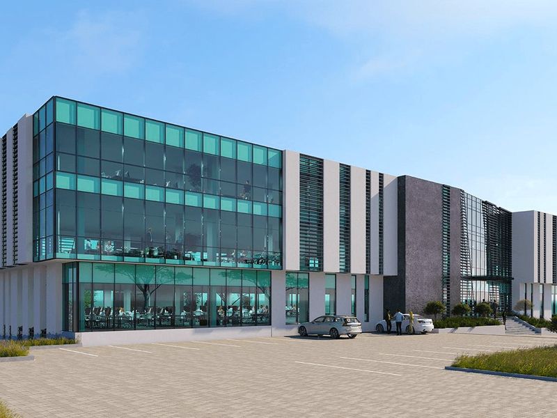 Modern multi-story commercial office building featuring extensive glass curtain walls, stone cladding, and a spacious paved parking area.