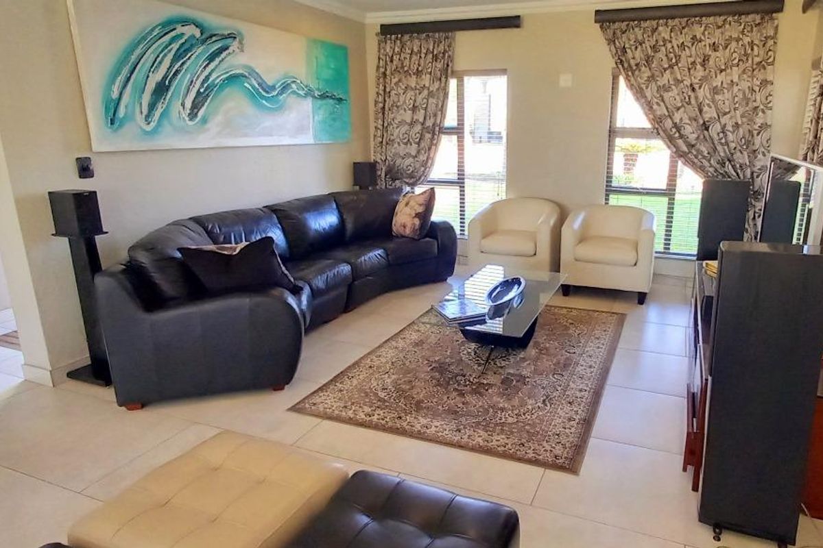 A spacious living room featuring neutral tiled flooring, large windows with natural light, and coved ceiling detailing.