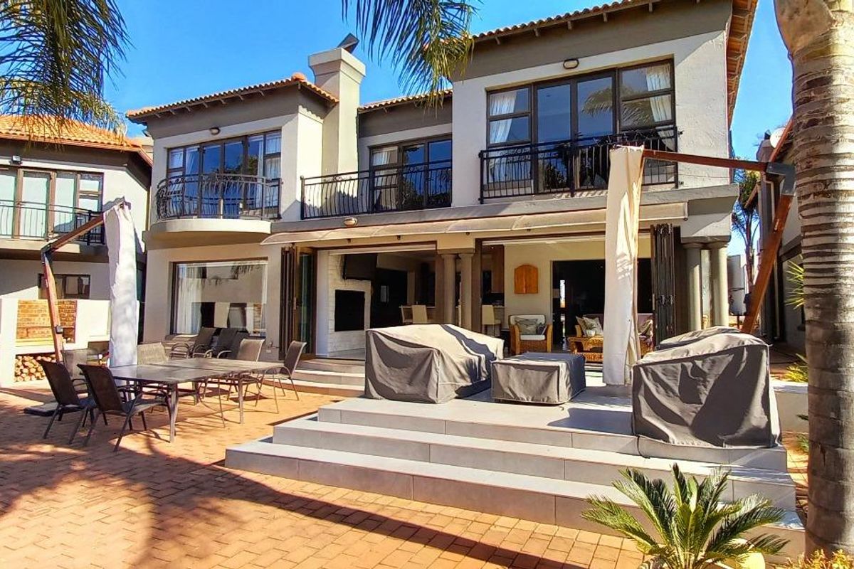 Spacious rear exterior featuring a paved patio area, raised tiled terrace, and multi-level balconies with wrought iron railings overlooking the garden.