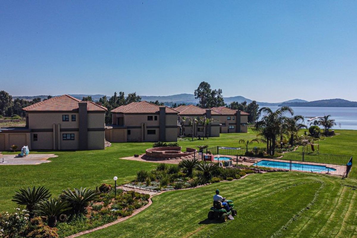 Aerial view of a residential apartment complex featuring landscaped gardens, a swimming pool, and scenic waterfront views.