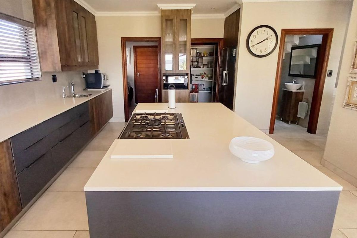 Modern kitchen featuring a large central island with a gas hob, stone countertops, ample cabinetry, and an adjacent walk-in pantry.