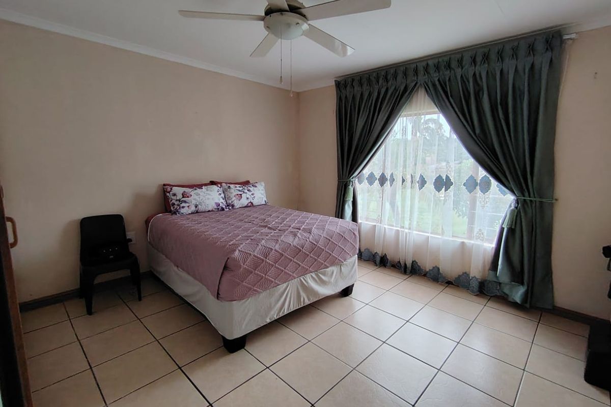 A standard bedroom featuring tiled flooring, a ceiling fan, and large windows with curtain rails, offering a functional and neutral living space.
