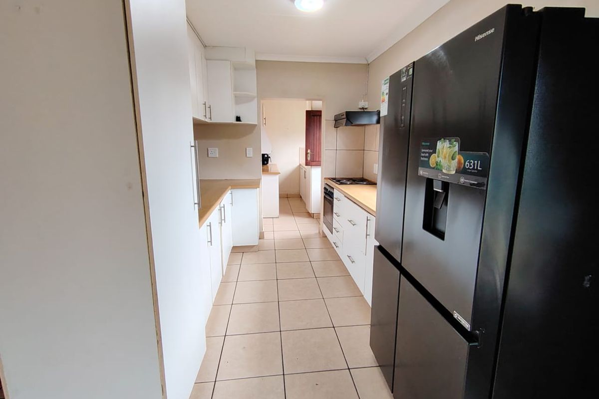 A functional galley-style kitchen featuring white cabinetry, laminate countertops, built-in oven, hob, and extractor fan, with tiled flooring throughout.