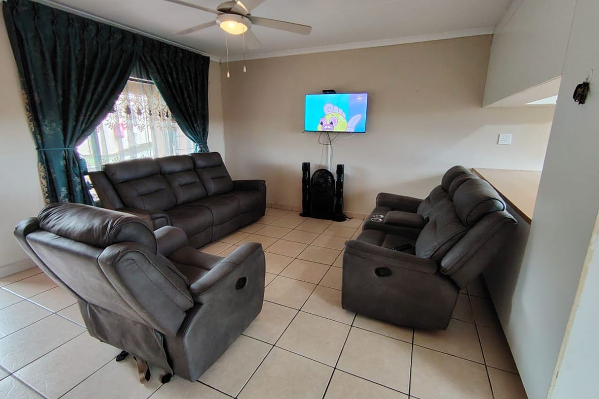 A living room area featuring tiled flooring, a ceiling fan, and an open-plan layout connecting to the kitchen breakfast bar.