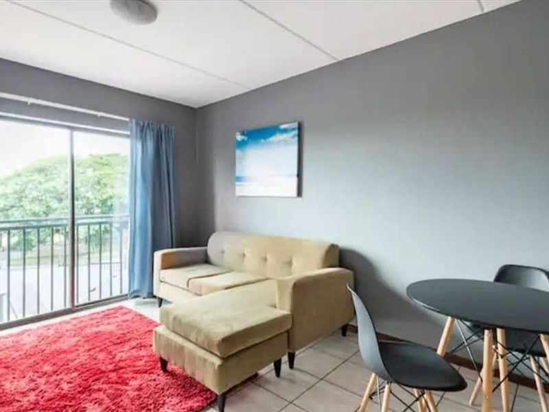 A living area featuring tiled flooring and a sliding glass door that opens onto a balcony with outdoor views.