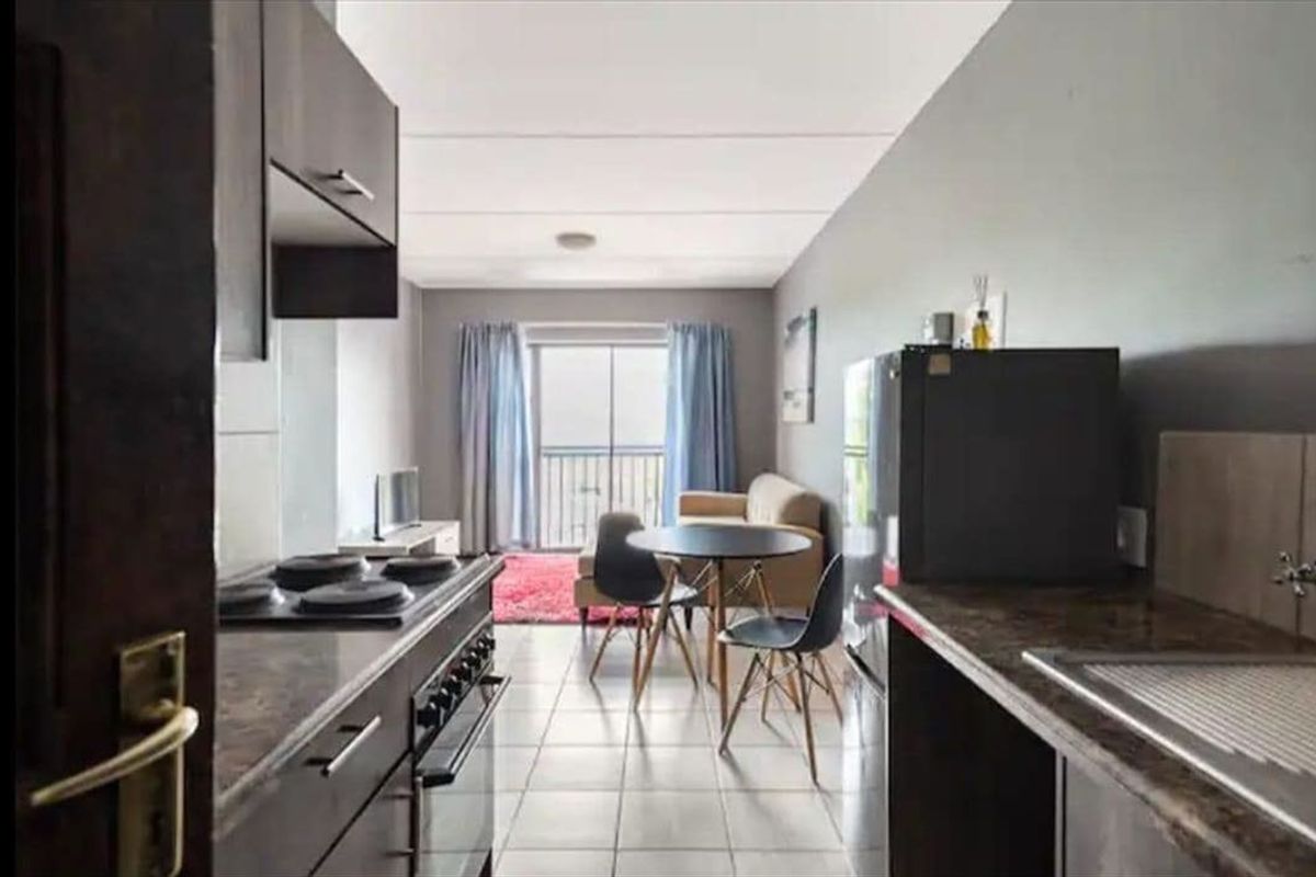 Open-plan kitchen and living area featuring tiled flooring, built-in cabinetry, and a sliding door leading to a balcony.