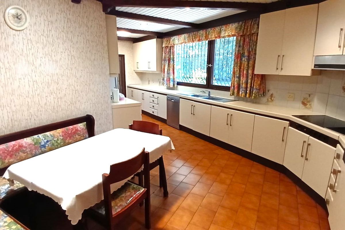 Spacious kitchen featuring extensive built-in cabinetry, integrated appliances, tiled flooring, and exposed timber ceiling beams, offering a functional layout with a dedicated dining area.