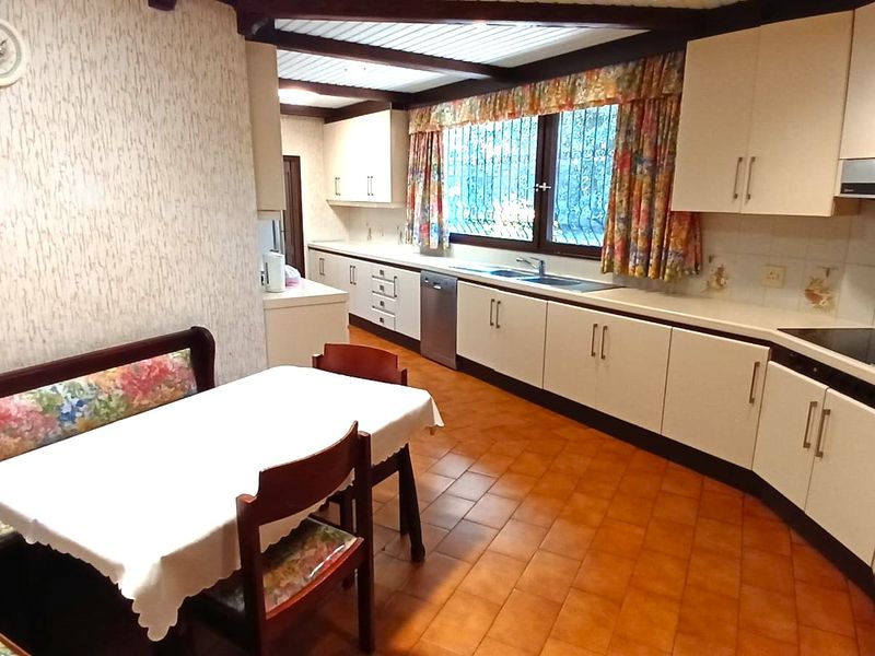 Spacious kitchen featuring extensive built-in cabinetry, integrated appliances, tiled flooring, and exposed timber ceiling beams, offering a functional layout with a dedicated dining area.
