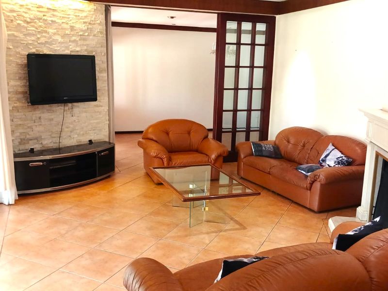 Spacious living room featuring a stone accent wall, fireplace mantel, and tiled flooring, with glass french doors leading to an adjacent area.