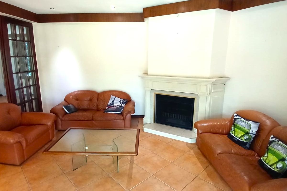 Spacious living room featuring a central fireplace with a decorative mantelpiece, tiled flooring, and timber crown molding, providing a classic foundation for updates.