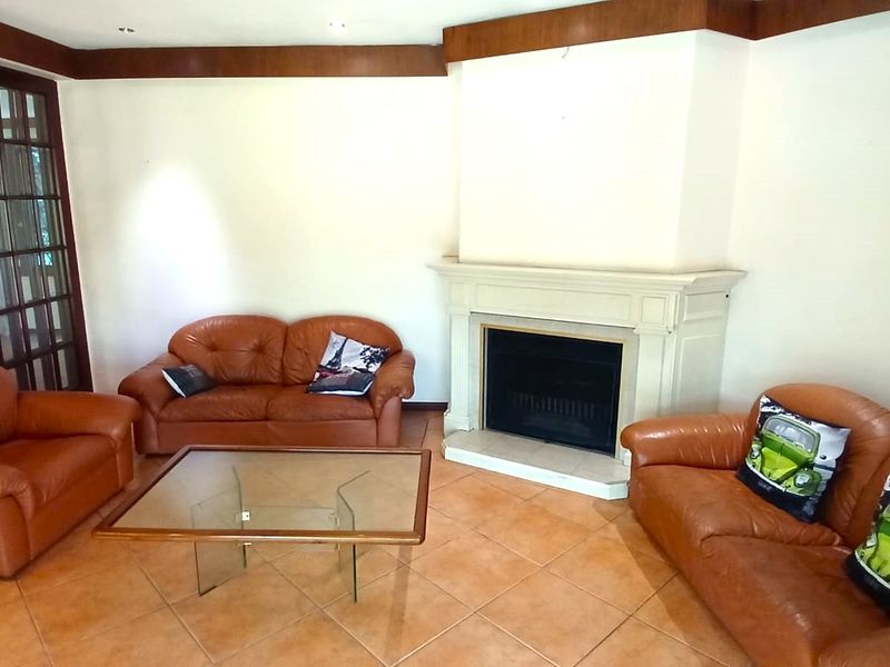 Spacious living room featuring a central fireplace with a decorative mantelpiece, tiled flooring, and timber crown molding, providing a classic foundation for updates.