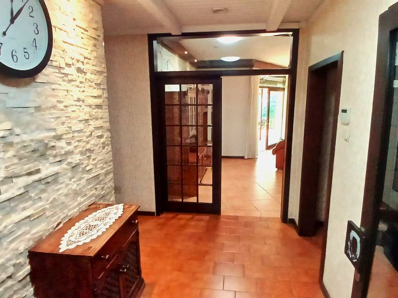 A welcoming hallway featuring a textured stone feature wall, terracotta floor tiles, and exposed ceiling beams leading into the main living area.