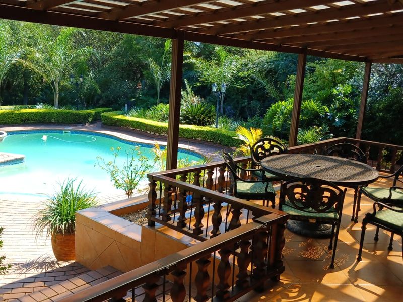Covered timber patio overlooking a landscaped garden and swimming pool area, featuring tiled flooring and a classic timber balustrade.