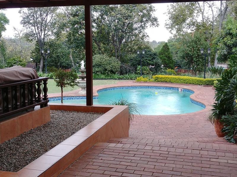 A covered patio overlooking a swimming pool and landscaped garden, featuring brick paving and a built-in tiled planter box.