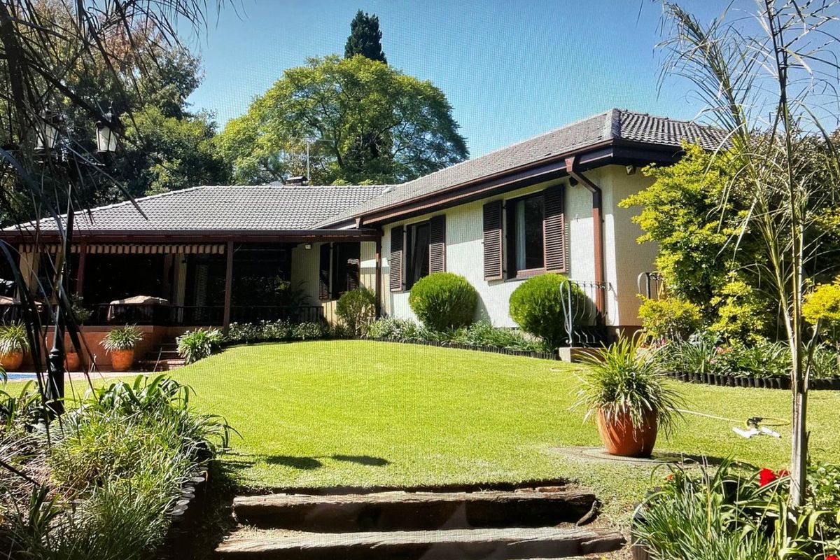A well-maintained rear exterior view of the house featuring a covered patio, timber shutters, and a landscaped garden with tiered steps.