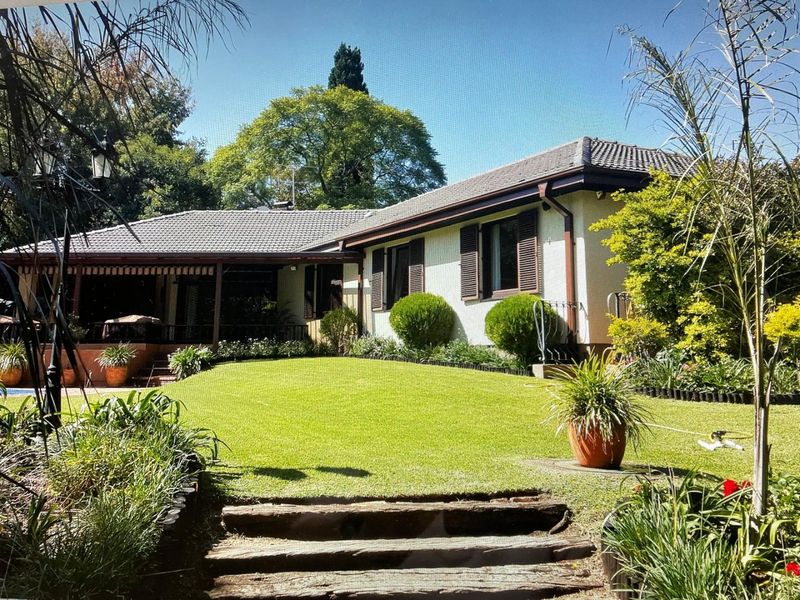 A well-maintained rear exterior view of the house featuring a covered patio, timber shutters, and a landscaped garden with tiered steps.