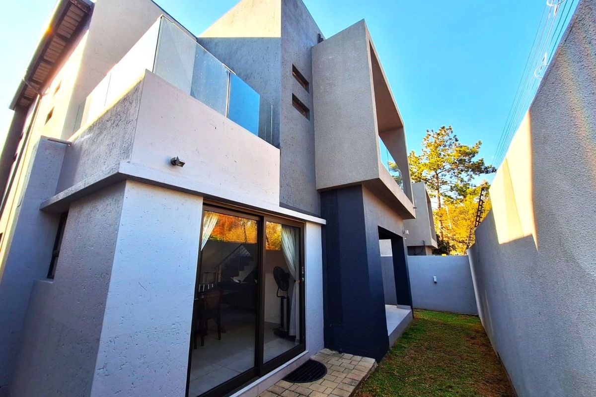 Rear view of a modern townhouse featuring a paved walkway, glass balcony balustrades, and sliding door access to the interior living space.