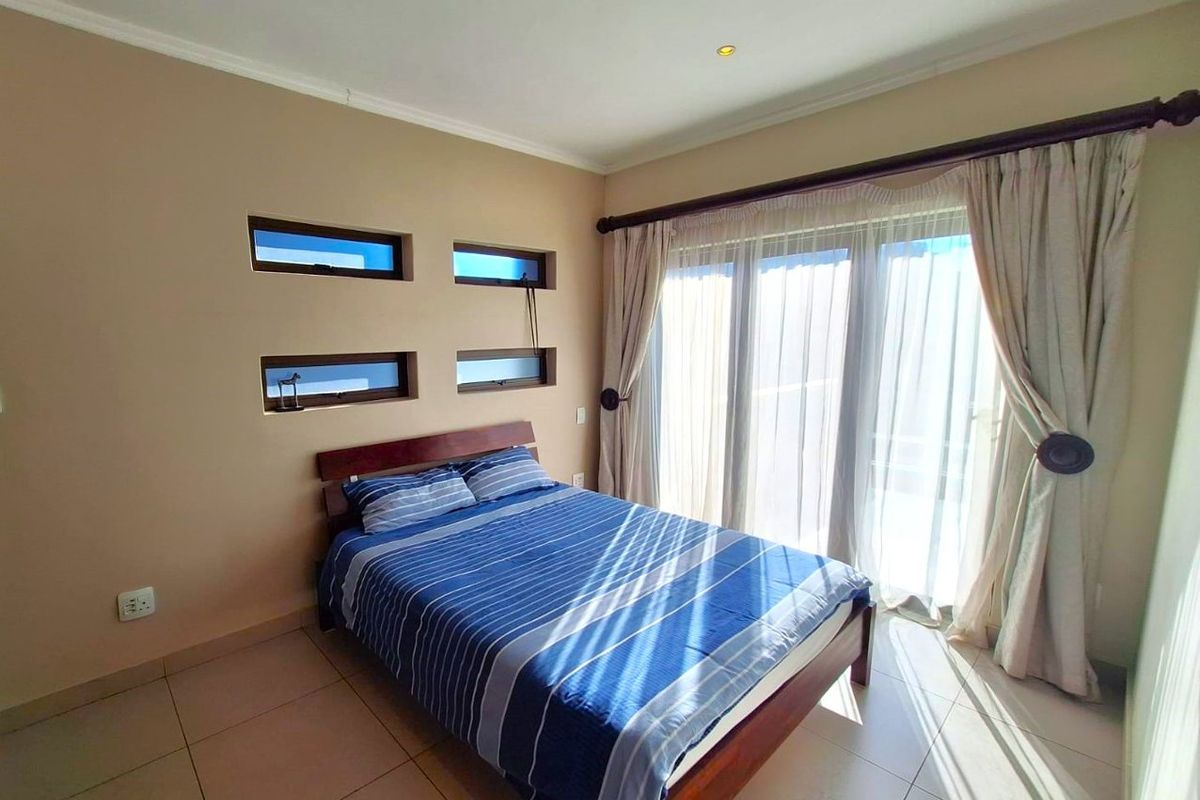 A bright bedroom featuring tiled flooring, unique feature windows, and a sliding glass door providing access to the outdoors.