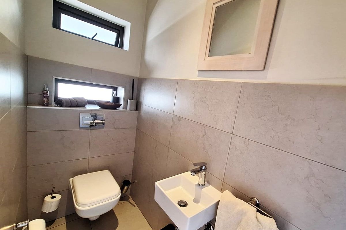 A modern guest bathroom featuring a wall-mounted toilet, a compact wall-mounted basin with chrome fixtures, and neutral floor-to-ceiling tiling.