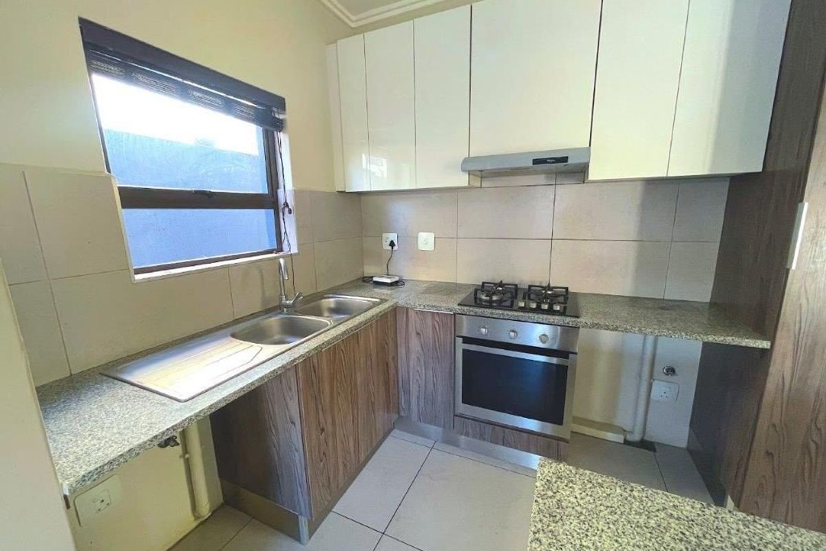 A functional kitchen featuring granite countertops, built-in oven with gas hob, extractor fan, and ample cabinetry, finished with neutral tiled flooring and backsplash.