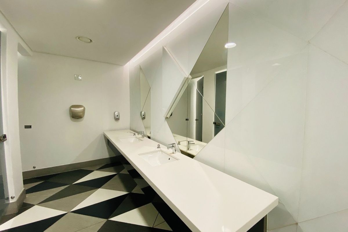 Modern commercial bathroom featuring a sleek double vanity with integrated sinks, geometric wall mirrors, and contemporary patterned floor tiling.