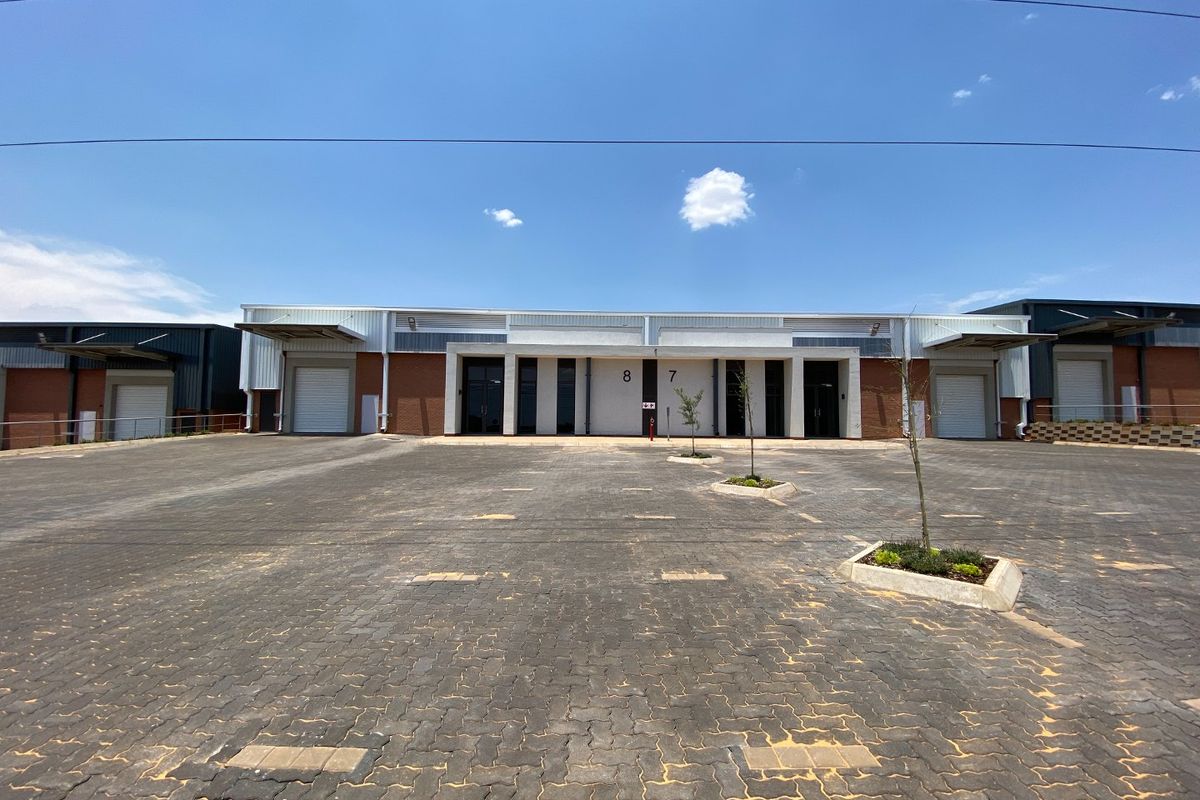Front elevation of an industrial warehouse complex featuring paved yard space, roller shutter doors, and modern brick and metal construction.