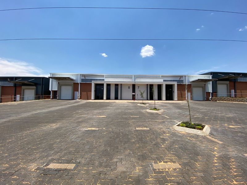 Front elevation of an industrial warehouse complex featuring paved yard space, roller shutter doors, and modern brick and metal construction.