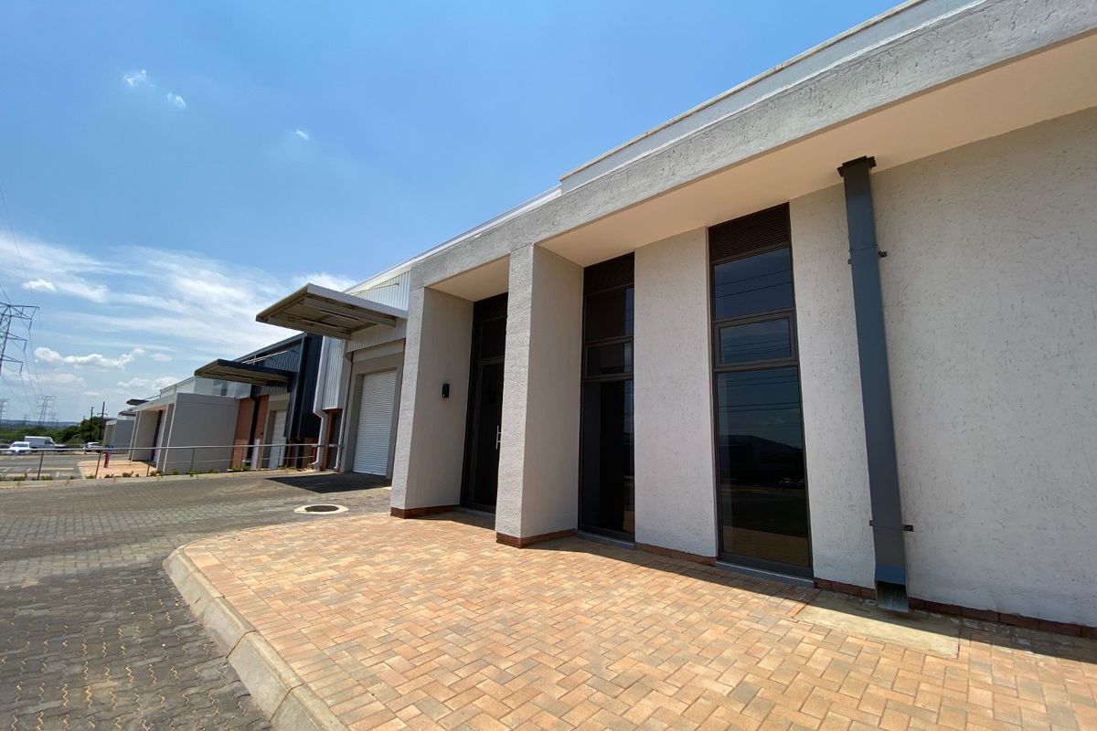 Modern industrial unit exterior featuring a paved driveway, roller shutter door, and clean architectural lines with large aluminium-framed windows.